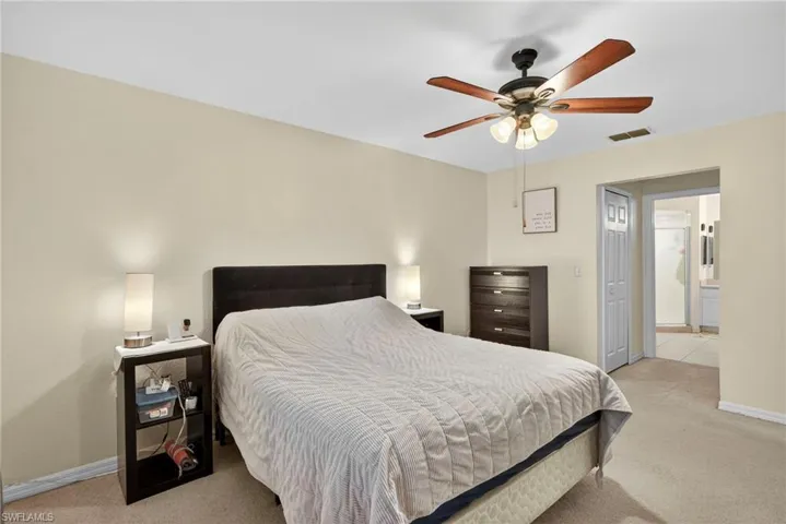 Bedroom featuring light carpet, a closet, ceiling fan, and ensuite bath