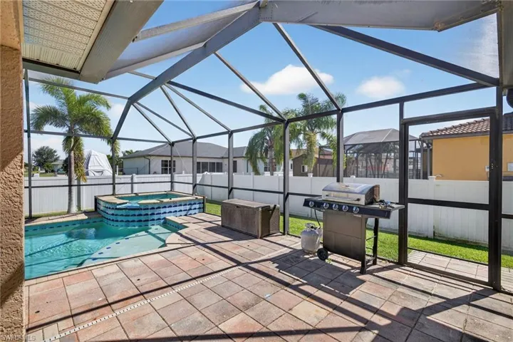 Fenced backyard featuring glass enclosure, area for grilling, a sunroom, a pool with connected hot tub, and a patio area
