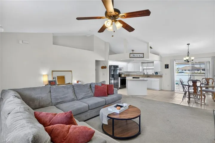 Living area with a chandelier, light colored carpet, a ceiling fan, light tile patterned flooring, and high vaulted ceiling