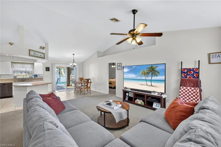 Living room with light colored carpet, light tile patterned floors, high vaulted ceiling, a chandelier, and ceiling fan