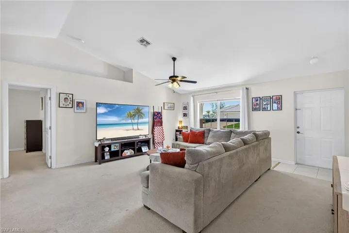 Living room featuring lofted ceiling, ceiling fan, and light carpet