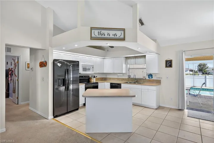 Kitchen featuring black appliances, white cabinetry, a center island, light tile patterned flooring, and light countertops