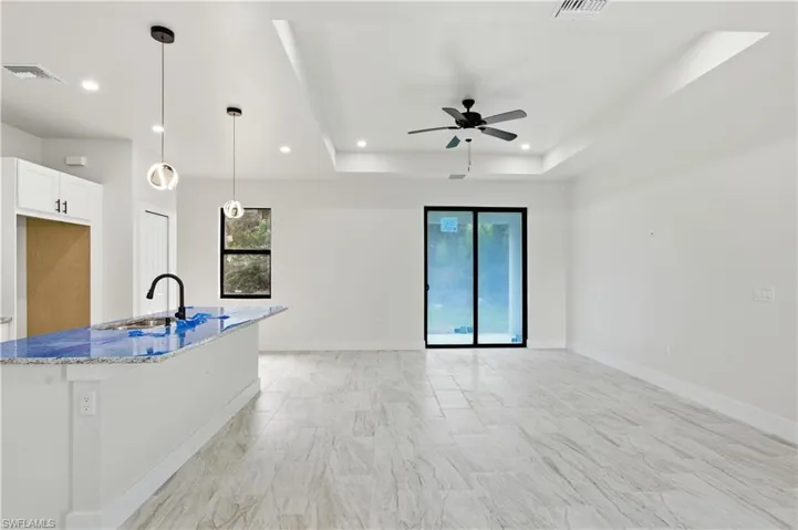Kitchen with pendant lighting, light stone counters, a raised ceiling, a ceiling fan, and white cabinetry