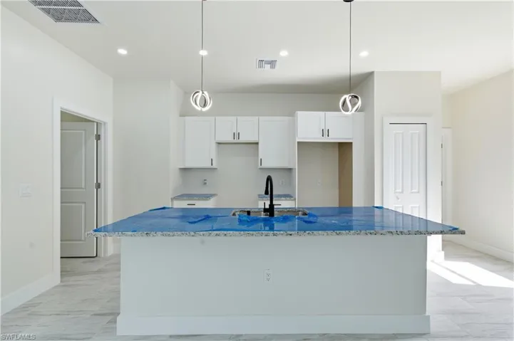 Kitchen featuring light stone countertops, hanging light fixtures, an island with sink, and white cabinetry