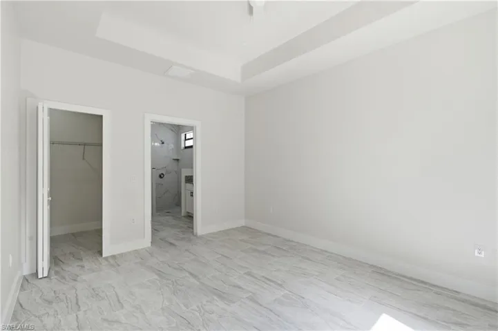 Unfurnished bedroom featuring a walk in closet, ensuite bathroom, and a tray ceiling
