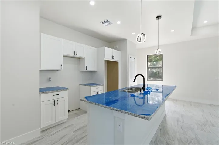 Kitchen featuring light stone counters, white cabinets, a kitchen island with sink, pendant lighting, and a kitchen bar