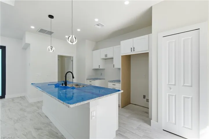 Kitchen with white cabinetry, a center island with sink, light stone countertops, decorative light fixtures, and a kitchen bar