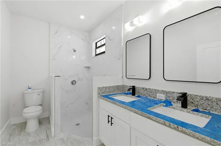 Bathroom with double vanity, a marble finish shower, light marble finish flooring, and recessed lighting