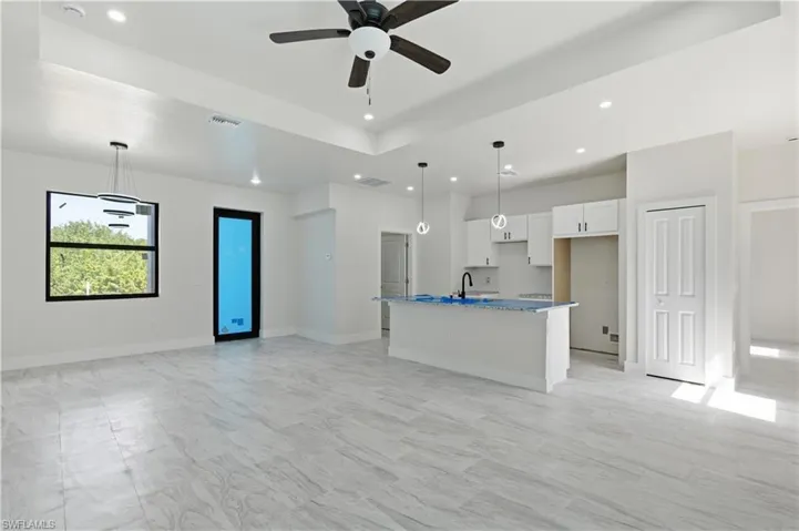Kitchen with white cabinets, an island with sink, hanging light fixtures, open floor plan, and a ceiling fan