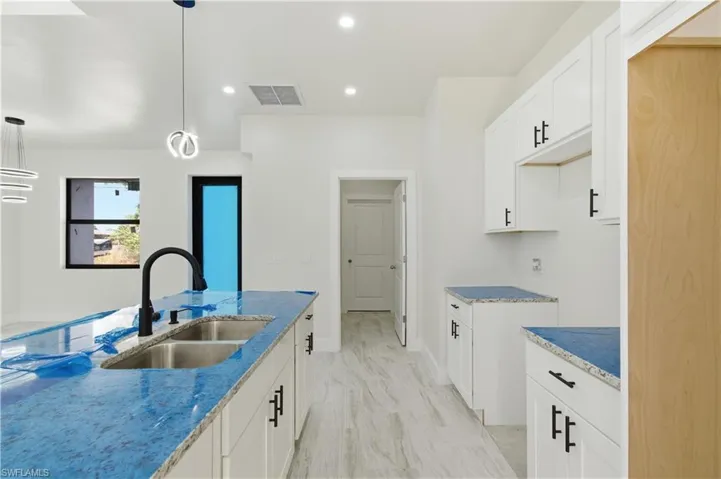 Kitchen with white cabinets, hanging light fixtures, and light stone countertops