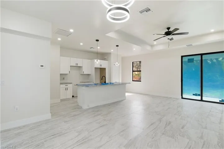 Kitchen featuring white cabinetry, ceiling fan, light stone countertops, pendant lighting, and a center island with sink