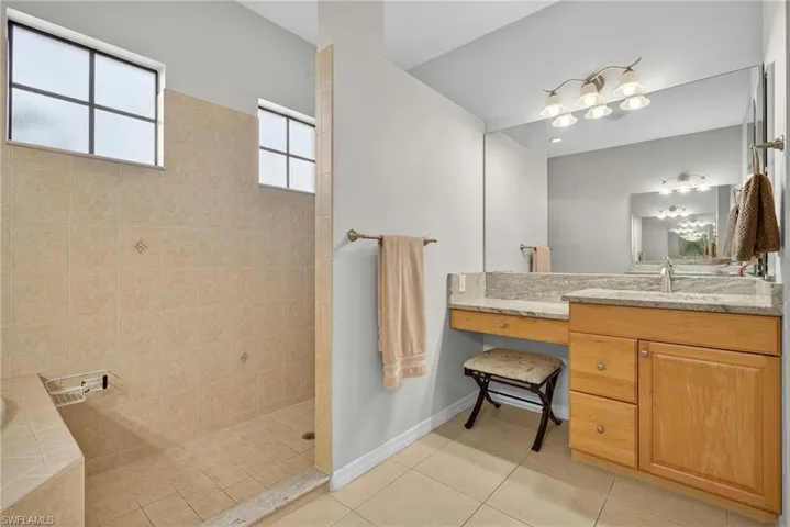 Full bath featuring dual vanity, walk-in shower, soaking tub, and light tile flooring.