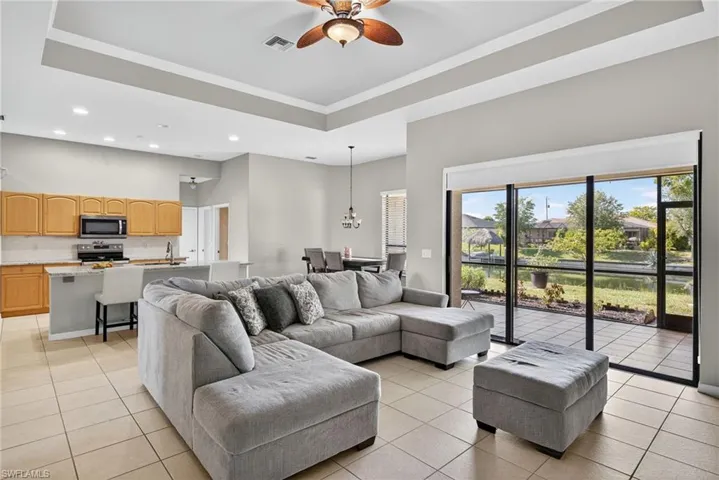 Spacious living room with raised ceiling, ceiling fan, crown molding, recessed lighting, and a decorative chandelier.