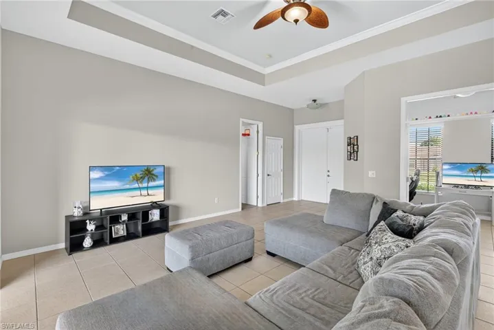 Flexible living space with raised ceiling, ceiling fan, crown molding, and light tile flooring throughout.