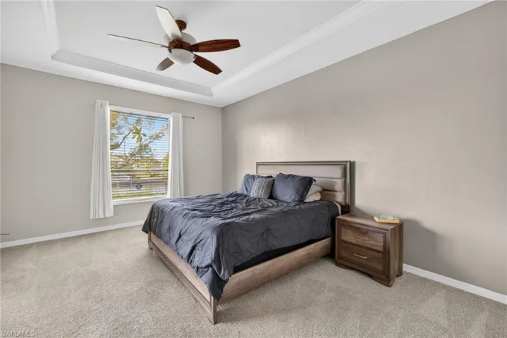 Carpeted primary bedroom with tray ceiling, ceiling fan, and crown molding. A quiet retreat.