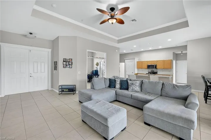 Open-concept living area with raised ceiling, crown molding, ceiling fan, and abundant natural light.
