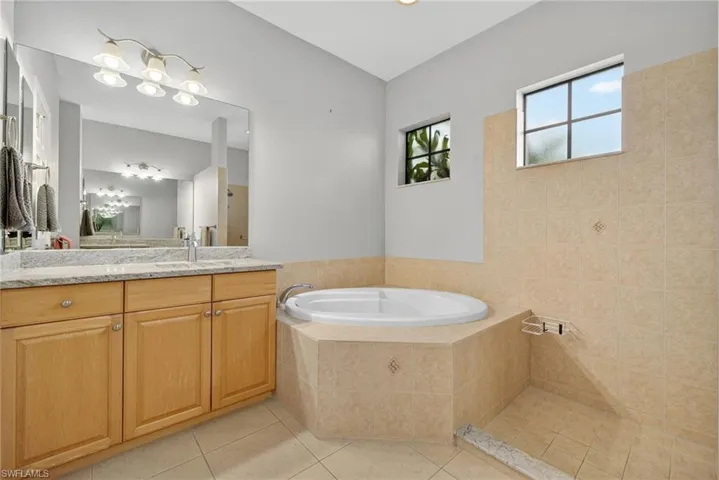 Full primary bath with soaking tub, vanity, light tile flooring, and a designer chandelier.