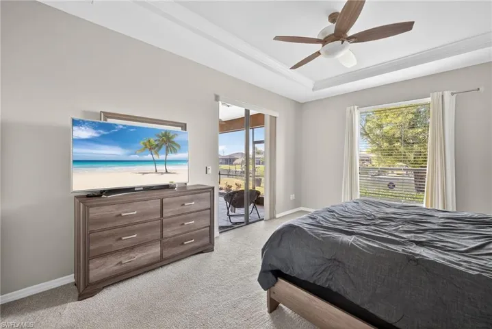 Primary bedroom featuring a tray ceiling, multiple windows, direct lanai access, and light carpet.