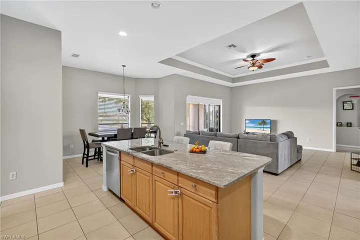 Open kitchen with raised ceiling, Level 4 River White granite, pendant and recessed lighting, and light tile flooring. Built for entertaining.
