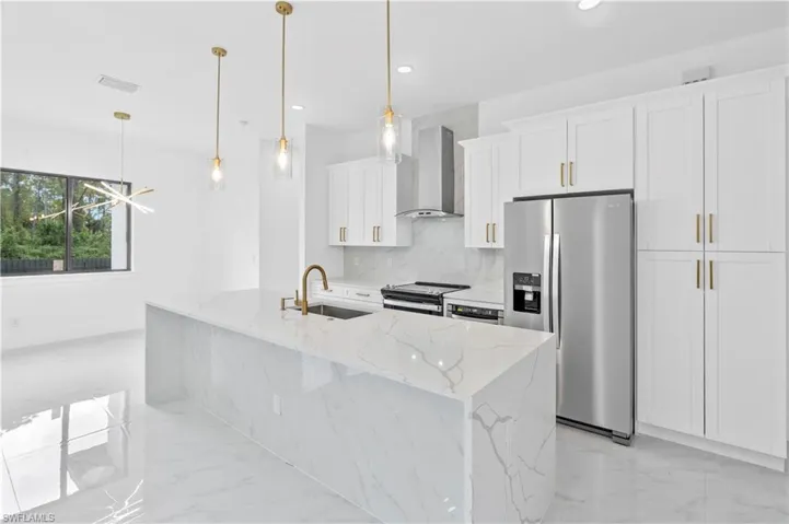 Kitchen with wall chimney exhaust hood, sink, white cabinetry, appliances with stainless steel finishes, and a center island with sink
