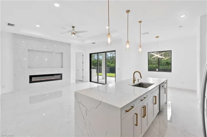 Kitchen featuring white cabinets, light stone countertops, hanging light fixtures, and a wealth of natural light