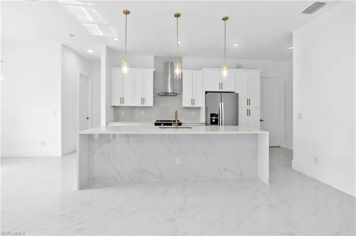 Kitchen featuring a large island with sink, wall chimney exhaust hood, white cabinetry, and stainless steel refrigerator with ice dispenser