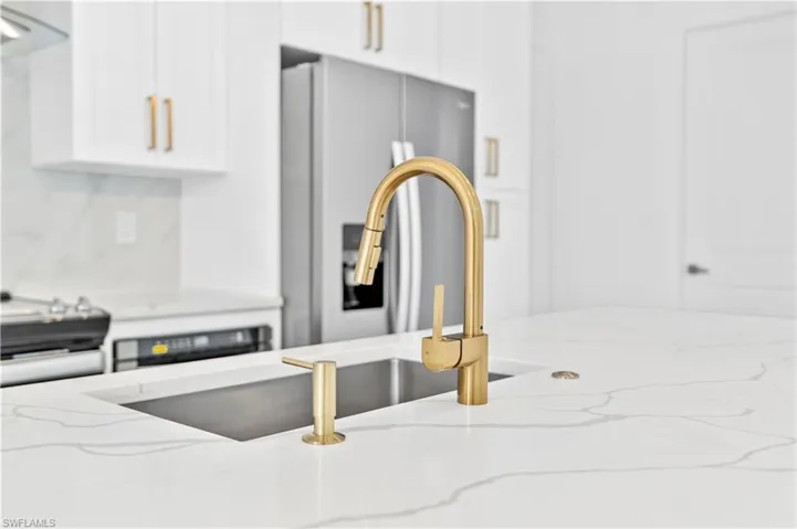 Interior details featuring stainless steel fridge, light stone counters, decorative backsplash, and white cabinets
