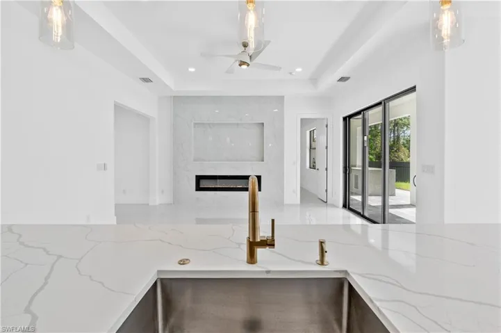 Kitchen with pendant lighting, light stone countertops, sink, and a raised ceiling