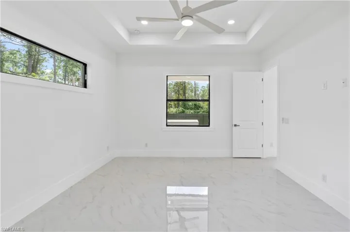 Empty room featuring ceiling fan, a tray ceiling, and a wealth of natural light