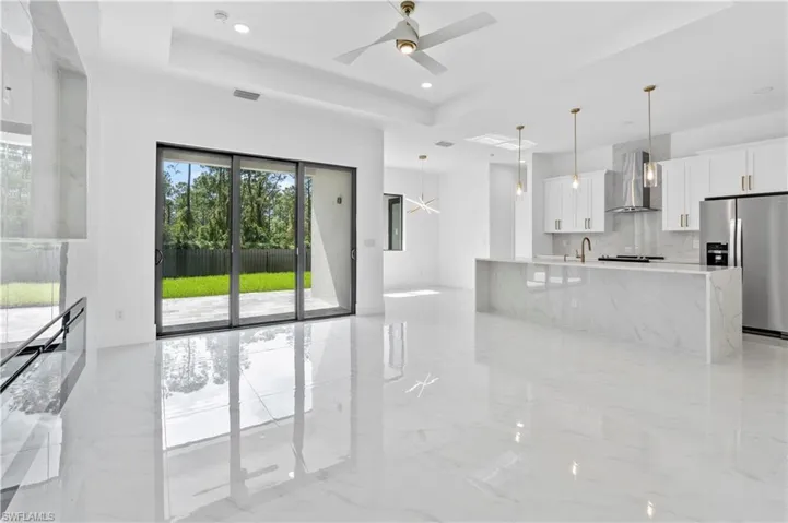 Kitchen with white cabinets, wall chimney exhaust hood, decorative light fixtures, stainless steel refrigerator with ice dispenser, and decorative backsplash
