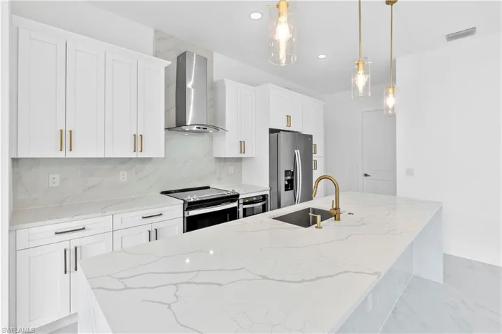 Kitchen featuring sink, decorative light fixtures, wall chimney range hood, white cabinetry, and stainless steel appliances