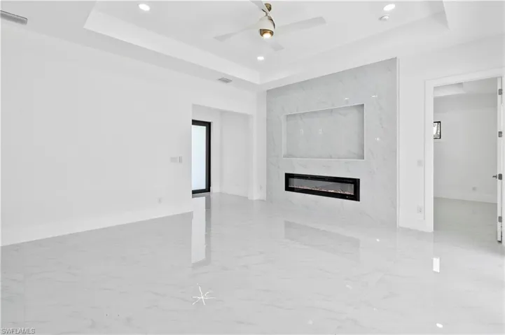 Unfurnished living room with a premium fireplace, ceiling fan, and a raised ceiling