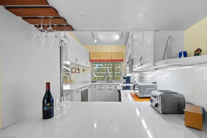 Kitchen featuring light stone countertops, white cabinetry, sink, rail lighting, and stainless steel appliances