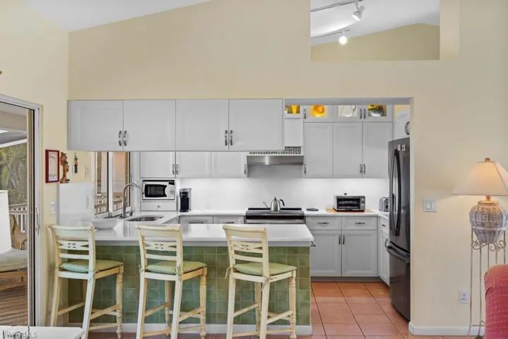 Kitchen featuring a kitchen breakfast bar, stainless steel appliances, light tile patterned floors, white cabinetry, and lofted ceiling