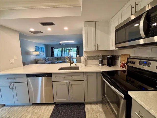 Kitchen with stainless steel appliances, light wood-style floors, gray cabinetry, backsplash, and recessed lighting