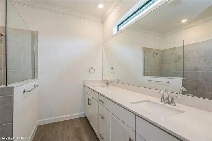 Full bath featuring a walk in shower, ornamental molding, dark wood-style flooring, and double vanity