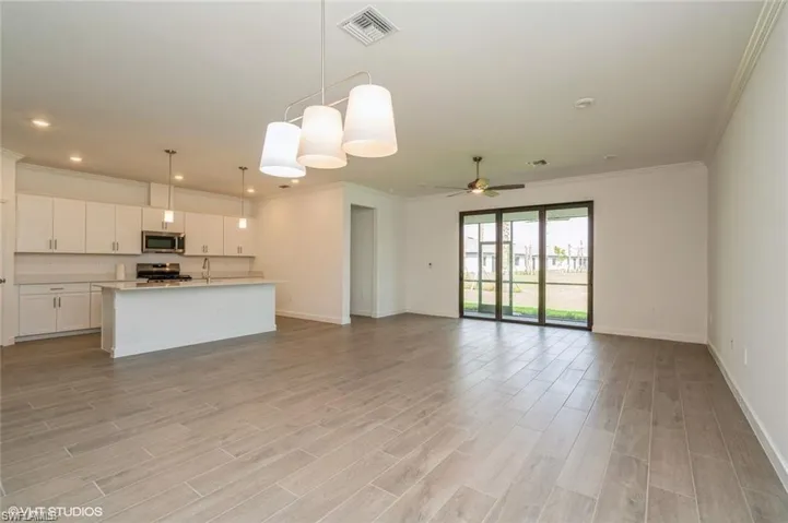Kitchen with decorative light fixtures, white cabinetry, open floor plan, an island with sink, and ornamental molding