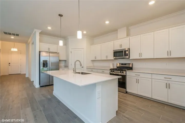 Kitchen with stainless steel appliances, ornamental molding, wood tiled floors, white cabinets, and hanging light fixtures