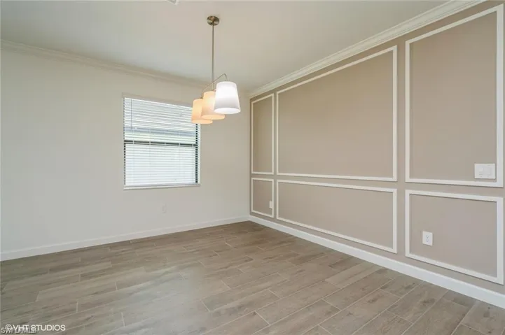 Unfurnished dining area featuring ornamental molding, light wood-style floors, and a decorative wall
