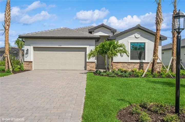 View of front of property with stone siding, decorative driveway, a front yard, an attached garage, and stucco siding