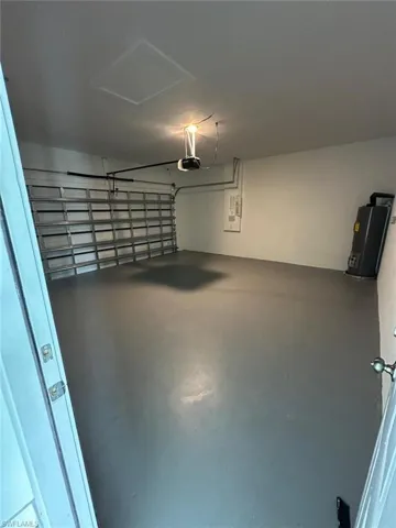 Garage featuring electric water heater, electric panel, and a garage door opener