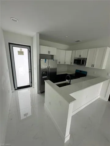Kitchen with light marble finish floors, white cabinets, stainless steel appliances, a peninsula, and light stone counters