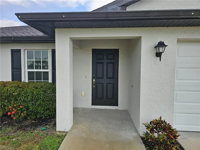 Inviting entryway featuring a paneled front door, stucco exterior, and an exterior wall lantern
