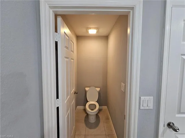 Powder room featuring a white toilet, neutral wall paint, and tiled flooring