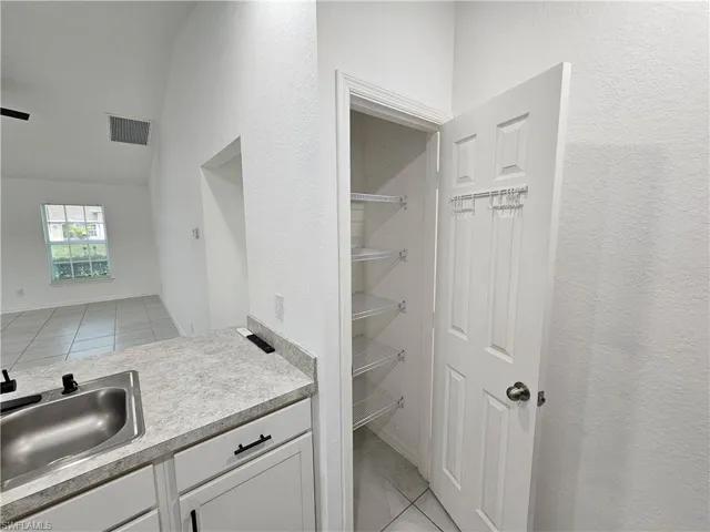 Kitchenette featuring a stainless steel sink, light gray countertop, white cabinetry with matte black hardware, and an adjacent pantry with wire shelving