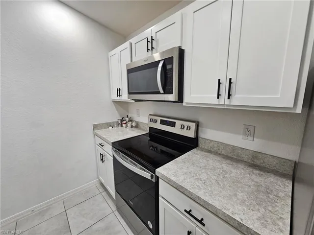 Kitchen featuring white shaker-style cabinetry with matte black hardware, stone-finish countertops, stainless steel microwave, and a black electric range
