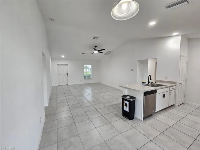 Spacious open-concept living area featuring light-toned tile flooring, vaulted ceilings, and recessed lighting