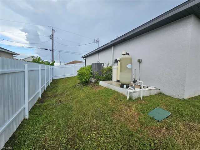 Exterior side yard featuring a white vinyl fence, green lawn, and a stucco-textured wall