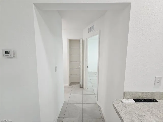 Hallway with light gray square tile flooring, leading to a closet with built-in shelving, and a separate room beyond