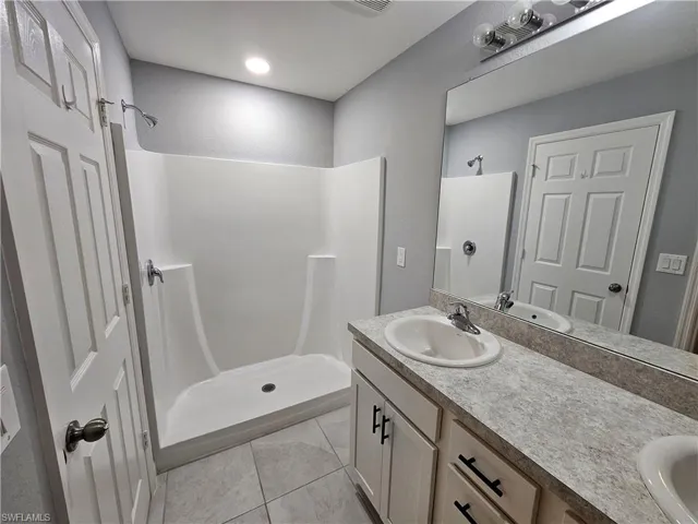 Bathroom featuring a dual-sink vanity with a speckled countertop, a large mirror, and a built-in shower stall with chrome fixtures